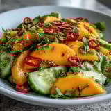 Colorful mango salad in a white bowl, with red bell pepper, red onion, cucumber, and fresh cilantro garnish.