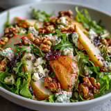 Fresh Arugula and Pear Bowl topped with creamy blue cheese and toasted walnuts on a rustic wooden table.