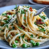 Creamy lemon butter pasta with peas and Parmesan in a skillet, garnished with fresh parsley and extra cheese.  