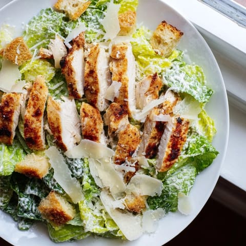 Close-up of Chicken Caesar Salad featuring creamy dressing drizzled over fresh lettuce and savory toppings.