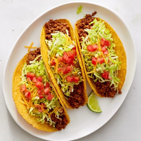 Freshly prepared Beef Tacos filled with seasoned beef, topped with sour cream and cilantro on a plate.