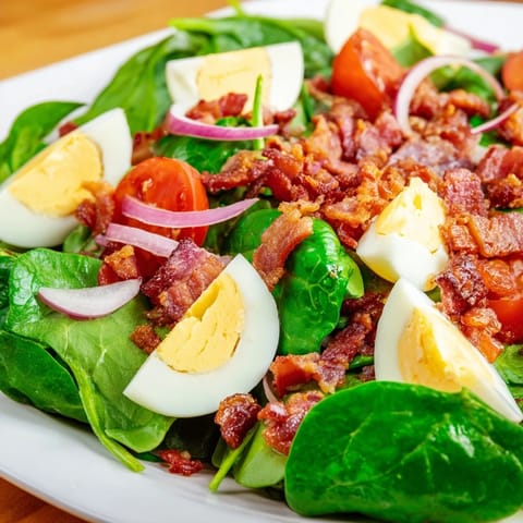 Spinach Salad with Bacon featuring fresh baby spinach, golden bacon pieces, sliced hard-boiled eggs, and a honey Dijon vinaigrette served in a white salad bowl.