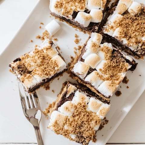 Cut into a gooey S'mores Bar revealing melted chocolate and toasted marshmallow layers, stacked on a dessert plate ready to be served.