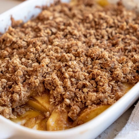 Classic Apple Crumble dessert served warm with a scoop of vanilla ice cream melting over the top.