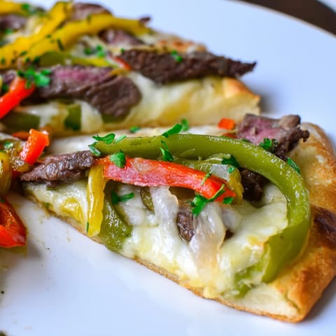 A close-up of a slice of Philly Cheesesteak Pizza being lifted, revealing tender ribeye steak and gooey cheese stretches.