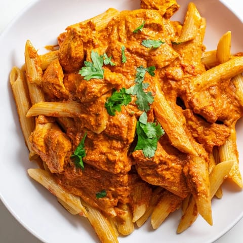 Steaming plate of Chicken Tikka Pasta garnished with fresh cilantro, blending Indian spices with Italian pasta for a fusion dinner.  