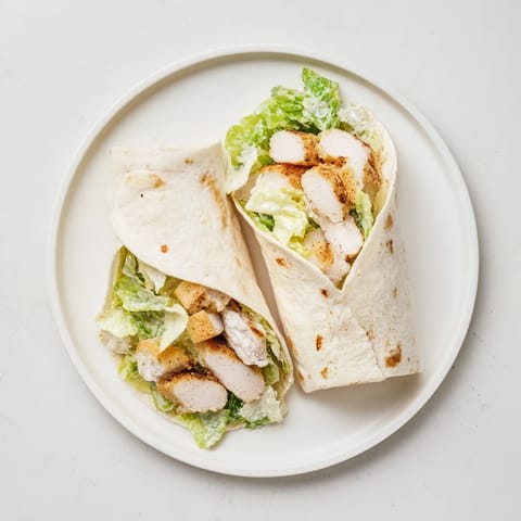 Two Caesar Chicken Salad Wraps sliced in half, revealing layers of grilled chicken, romaine, croutons, and parmesan on a rustic plate.