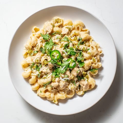 Green Chili Chicken Mac in a creamy skillet, garnished with cilantro and sliced jalapeños for extra zest.