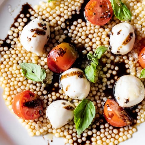 Fork-tender pearled couscous mingles with juicy cherry tomatoes and mozzarella balls in this vibrant Caprese Couscous Salad, drizzled with balsamic glaze.