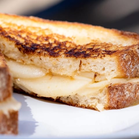 A buttery Smoked Gouda & Apple Grilled Cheese served with tomato soup on a rustic table for a cozy lunch.  