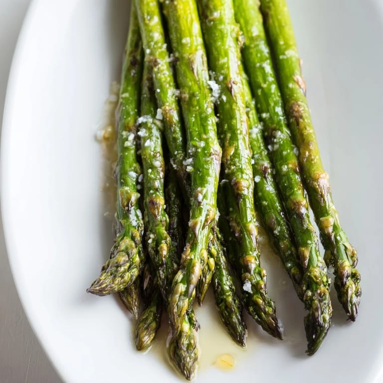 Fresh Grilled Asparagus topped with sea salt and bright lemon juice on a white plate.