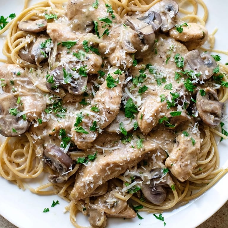 Steaming creamy mushroom chicken spaghettini in a skillet, showing a glossy sauce with mushrooms, spinach, and fresh herbs.