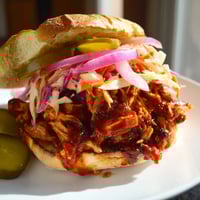 Smoky BBQ Chicken Sandwich stacked high with tender chicken, slaw, and pickles on a toasted bun.