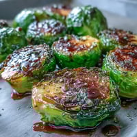 Golden-brown roasted Brussels sprouts with balsamic reduction, served on a white plate as a savory vegetarian side dish.