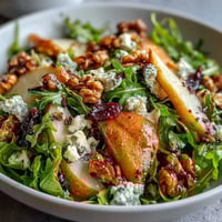 Fresh Arugula and Pear Bowl topped with creamy blue cheese and toasted walnuts on a rustic wooden table.