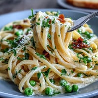 Creamy lemon butter pasta with peas and Parmesan in a skillet, garnished with fresh parsley and extra cheese.  
